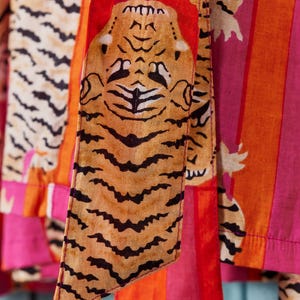 May include: Close-up of colorful fabric with tiger print and stripes. The fabric features a tiger face and stripes in shades of orange, pink, and white. The tiger print is in shades of brown and black.