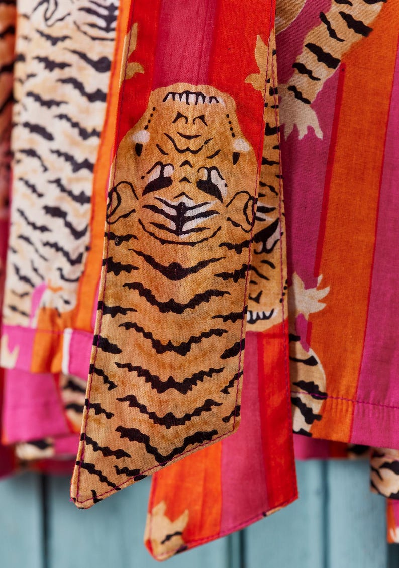 May include: Close-up of colorful fabric with tiger print and stripes. The fabric features a tiger face and stripes in shades of orange, pink, and white. The tiger print is in shades of brown and black.