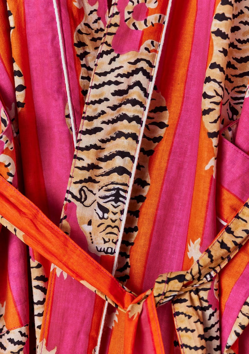 May include: A vibrant, striped robe in shades of pink and orange, featuring a tiger print. The robe has a matching belt and white trim. The design is bold and eye-catching, perfect for lounging or as a statement piece.