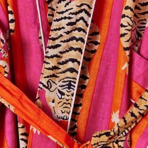 May include: A vibrant, striped robe in shades of pink and orange, featuring a tiger print. The robe has a matching belt and white trim. The design is bold and eye-catching, perfect for lounging or as a statement piece.
