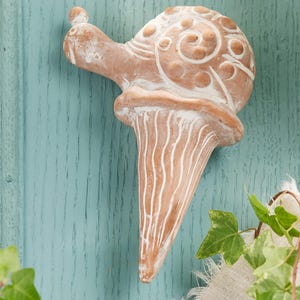 May include: A white ceramic snail sculpture with a detailed shell design. The snail is perched on a wooden surface with a light blue paint finish.