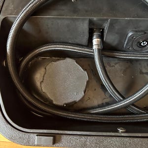 May include: Black plastic case with a black hose coiled inside. The case has a textured surface and a round, textured cap. The text "RIDEKIT" and a phone number are visible on the top of the case.
