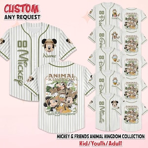 May include: White baseball jersey with green pinstripes, featuring Mickey Mouse in a safari hat. The jersey has "Mickey" down the side and "Animal Kingdom" on the back. The image also shows other character jerseys.