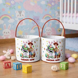 May include: Two white Easter baskets with red handles, featuring Buzz Lightyear and Woody from Toy Story. The baskets are decorated with Easter eggs, carrots, and stars. The text "CUSTOM NAME" is printed on the front.