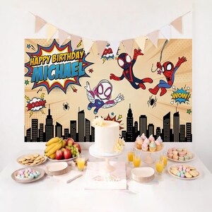 May include: A birthday party scene with a backdrop featuring Spider-Man characters and the text "Happy Birthday Michael." The table is set with a white cake, cupcakes, biscuits, fruit, and juice. A banner of pennants hangs above.