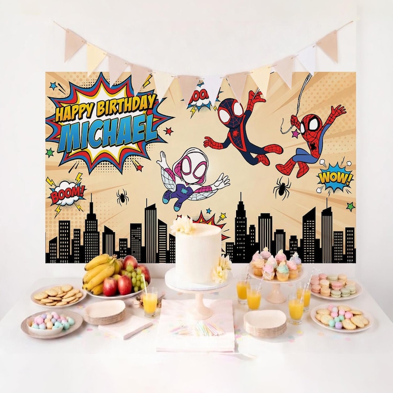 May include: A birthday party scene with a backdrop featuring Spider-Man characters and the text "Happy Birthday Michael." The table is set with a white cake, cupcakes, biscuits, fruit, and juice. A banner of pennants hangs above.
