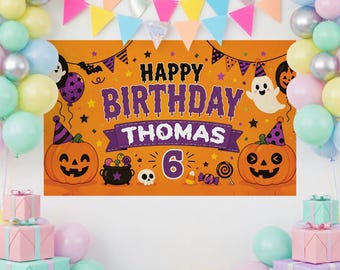May include: An orange Halloween-themed birthday banner featuring the text Happy Birthday Thomas 6, decorated with illustrations of two jack-o'-lanterns, a ghost, a cauldron, a skull, and candy, surrounded by pastel-colored balloons and bunting.