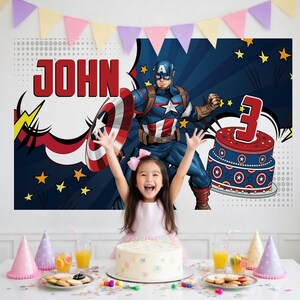May include: A birthday party scene with a young girl in a pink dress, arms raised, in front of a Captain America backdrop. The backdrop features the name "JOHN" and a cake with a "3" on top. A table is set with a cake, snacks, and party hats.