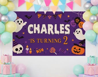 May include: A purple rectangular Halloween-themed party banner featuring the text CHARLES IS TURNING 2, surrounded by illustrations of ghosts, a skull, a jack-o'-lantern, bats, candy, and candles, framed by colorful balloons and bunting flags.