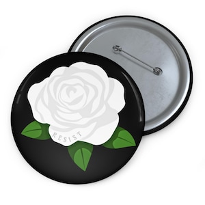 May include: A white ceramic mug with a black handle and the text "But First, Coffee" in a bold, black font. The mug is filled with a dark liquid, likely coffee, and sits on a light-colored surface.