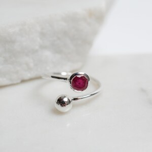 May include: A silver ring with a red gemstone and a silver ball on the band.