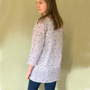 Peut inclure: Une chemise blanche à manches longues avec un imprimé floral gris. La chemise a une coupe ample et un col rond.