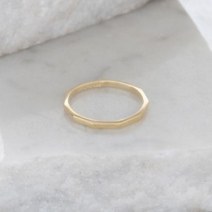 May include: A gold-colored ring with a faceted, octagonal design. The ring is simple and elegant.