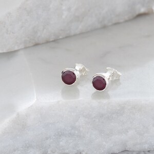 May include: A pair of silver stud earrings with round, dark red gemstones.