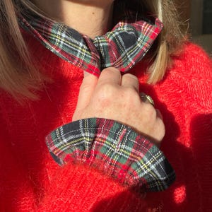May include: A red, fuzzy sweater with a plaid collar and cuffs. The plaid pattern includes black, green, red, and yellow. The collar is tied in a bow.