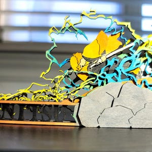 Może przedstawiać: Wielowarstwowa drewniana rzeźba przedstawiająca postać z mieczem, otoczoną żółtymi i niebieskimi błyskawicami. Podstawa zawiera napis "MENTIS" w wyciętym wzorze, z szarą strukturą przypominającą kamień po prawej stronie. Rzeźba stoi na ciemnej powierzchni.