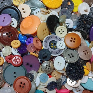 May include: A large collection of assorted sewing buttons in various shapes, sizes, and colors including brown, black, purple, orange, white, and blue. Some buttons feature four holes, two holes, or decorative patterns and embossed text.