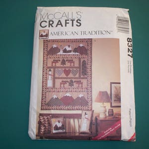 May include: A McCall's Crafts pattern titled "American Tradition" featuring a quilt design with mountains, houses, trees, and a snowman. The pattern includes the number 8327 and is for one envelope.