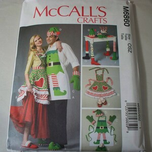 May include: A sewing pattern for elf-themed aprons. The pattern includes instructions for making a red and white striped apron with a heart, a green and white striped apron with a heart, and a green and white elf costume with a hat. The pattern is from McCall's Crafts and is size OSZ.