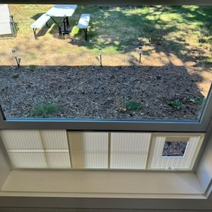 K&ouml;nnte beinhalten: Ein wei&szlig; gerahmtes Oberlicht mit Blick auf einen Garten. Der Garten verf&uuml;gt &uuml;ber einen Picknicktisch, St&uuml;hle und ein Blumenbeet. Das Oberlicht hat einen eingebauten, hellen, plissierten Sonnenschutz.