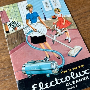 May include: Vintage advertisement for an Electrolux vacuum cleaner, Model G. The illustration depicts a woman in a blue top and black skirt using the vacuum, with a child and dog nearby. The cleaner is a light blue color.