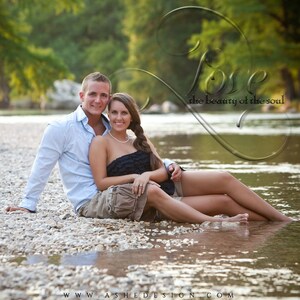May include: A couple poses for a photo in a shallow river bed. The woman is wearing a black strapless dress and the man is wearing a light blue button-down shirt and khaki shorts. The couple is sitting on a bed of small white rocks. The water is clear and shallow, and the riverbed is visible. The text "Love the beauty of the soul" is superimposed over the image.
