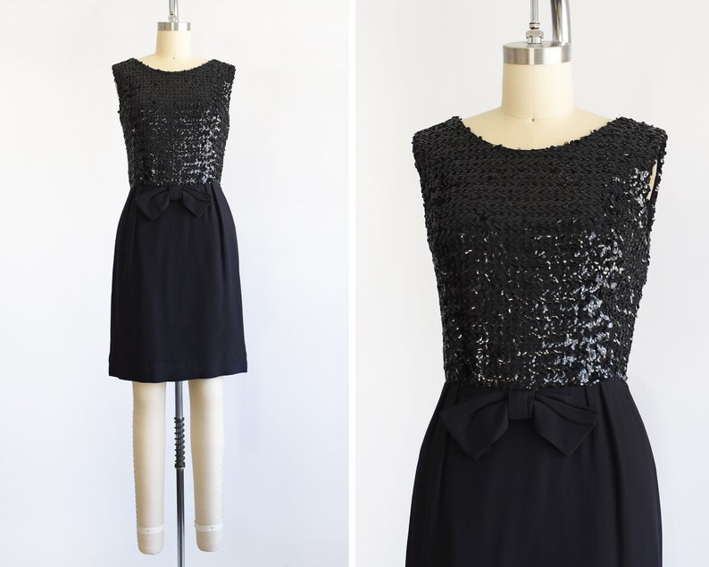 A vintage late 50s early 60s black dress that has a black sequin bodice, a bow at the waist, and a pencil skirt. The dress is modeled on a dress form