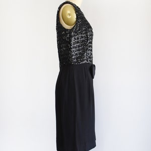 Side view of a vintage late 50s early 60s black dress that has a black sequin bodice, a bow at the waist, and a pencil skirt. The dress is modeled on a dress form