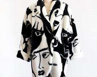 Peut inclure: Un manteau à manches longues présentant un motif contrasté noir et blanc de visages humains stylisés. Le vêtement possède un large col châle, une fermeture à un seul bouton sur le devant et des poignets repliés, avec une texture douce et pelucheuse.