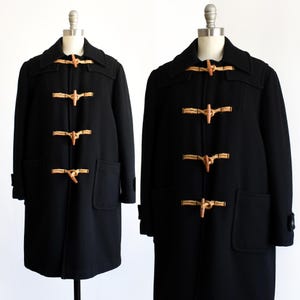 Könnte beinhalten: Zwei schwarze Dufflecoats, präsentiert auf Schaufensterpuppen. Jeder Mantel hat einen klassischen Knebelverschluss mit Holzknebeln und Seilschlaufen. Die Mäntel haben große Vordertaschen und einen Kragen. Ein klassisches Oberbekleidungsstück.