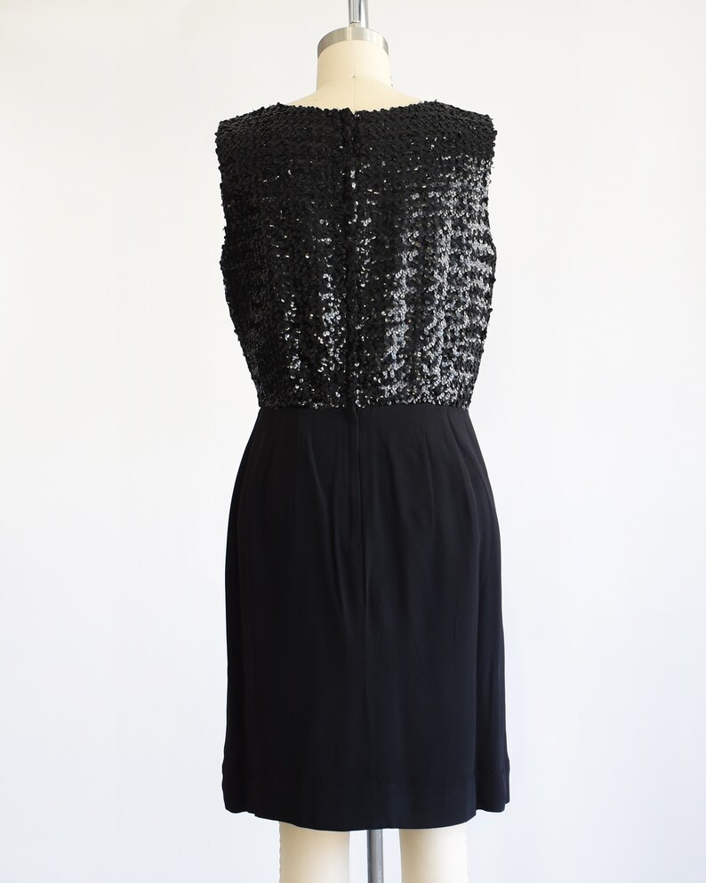Back view of a vintage late 50s early 60s black dress that has a black sequin bodice and a pencil skirt. The dress is modeled on a dress form