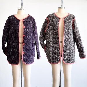 May include: Two quilted jackets on dress forms. One is dark purple with a white dot pattern, the other is black with a floral print. Both have a pink trim and matching pink buttons.