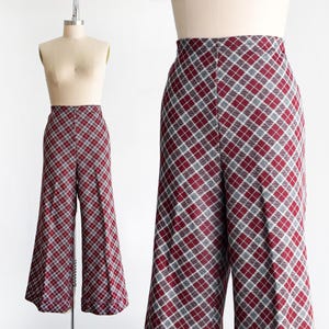 以下が含まれることがあります： 赤、グレー、白のチェック柄のワイドパンツ。マネキンに展示されています。生地は質感があり、チェック柄は左右対称です。