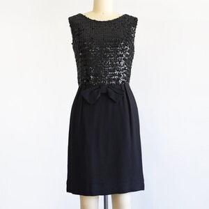 A vintage late 50s early 60s black dress that has a black sequin bodice, a bow at the waist, and a pencil skirt. The dress is modeled on a dress form