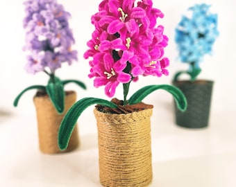 以下が含まれることがあります： 3つの鉢植えのヒヤシンスの花。花はふわふわのパイプクリーナーで作られています。ヒヤシンスはピンク、パープル、ブルーです。鉢は紐でできています。