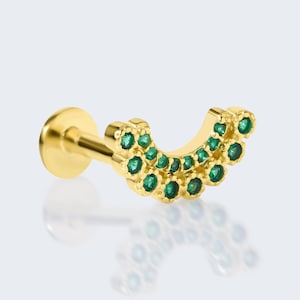 May include: A gold-colored earring with a curved design, adorned with small, round, green gemstones. The earring has a flat back and a post for piercing. The gemstones are arranged in a semi-circle pattern.