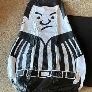 May include: Black and white inflatable referee figure with a stern expression. The figure is wearing a striped referee uniform with a black belt.