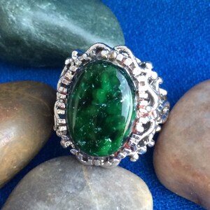 May include: A silver ring with a large, oval-shaped green gemstone set in a decorative filigree design.