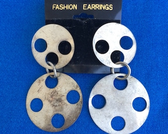 May include: A pair of silver tone earrings with a circle design. The earrings have multiple circles with cutouts. The earrings are on a black card with the text "FASHION EARRINGS".