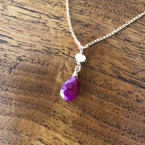 May include: A gold chain necklace with a teardrop-shaped ruby pendant and a small white pearl accent.