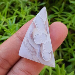 Puede incluir: Un cabujón de ágata blanca con forma triangular y un patrón de círculos y remolinos blancos y grises.