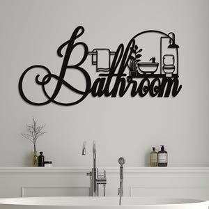May include: Black metal bathroom sign with the word "Bathroom" in a decorative script. The sign features silhouettes of bathroom fixtures and accessories, including a towel rack, plants, a toilet, and a bathtub.