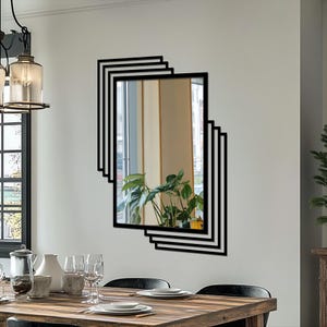 Peut inclure: Un miroir mural rectangulaire avec un cadre noir et un design superposé unique. Le miroir reflète une pièce avec une fenêtre et des plantes. Le miroir est monté sur un mur blanc dans une salle à manger.