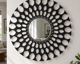 May include: A circular wall mirror featuring a black frame with a decorative, intricate cutout pattern consisting of repeating oval and petal-like shapes radiating outward from the central reflective glass surface in a symmetrical design.