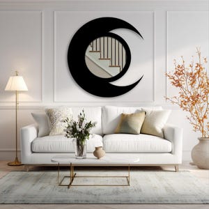 May include: A black crescent moon mirror hangs above a white sofa with decorative pillows. A marble coffee table with gold legs holds a vase of flowers and a small ceramic vase. A floor lamp and a large vase with branches complete the room.