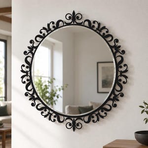 Puede incluir: Un espejo de pared redondo con un marco negro que presenta un diseño de volutas simétrico e intrincado. El borde decorativo incluye patrones curvos repetitivos y motivos de flor de lis que rodean la superficie de vidrio reflectante.