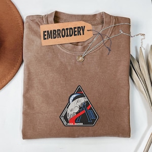 以下が含まれることがあります： 黒い持ち手と「But First, Coffee」の文字が黒い手書き風フォントで書かれた白いセラミックマグ。マグカップは白い表面に置かれています。