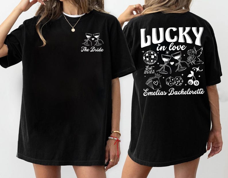 May include: Black t-shirt with white graphic designs. The front features two wine glasses and the text "The Bride". The back displays "LUCKY in love" with a disco ball, dice, cherries, and the text "Emelias Bachelorette".
