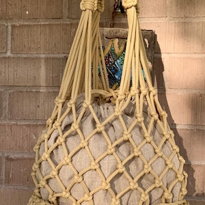Pode incluir: Uma bolsa tote de crochê bege com um design de rede. A bolsa tem um fundo grosso de crochê e alças compridas.