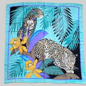 May include: A square scarf featuring a vibrant turquoise background with two leopards, yellow orchid flowers, and dark green palm leaves. The design includes purple accents and the text "loredano" printed in the bottom right corner of the fabric.